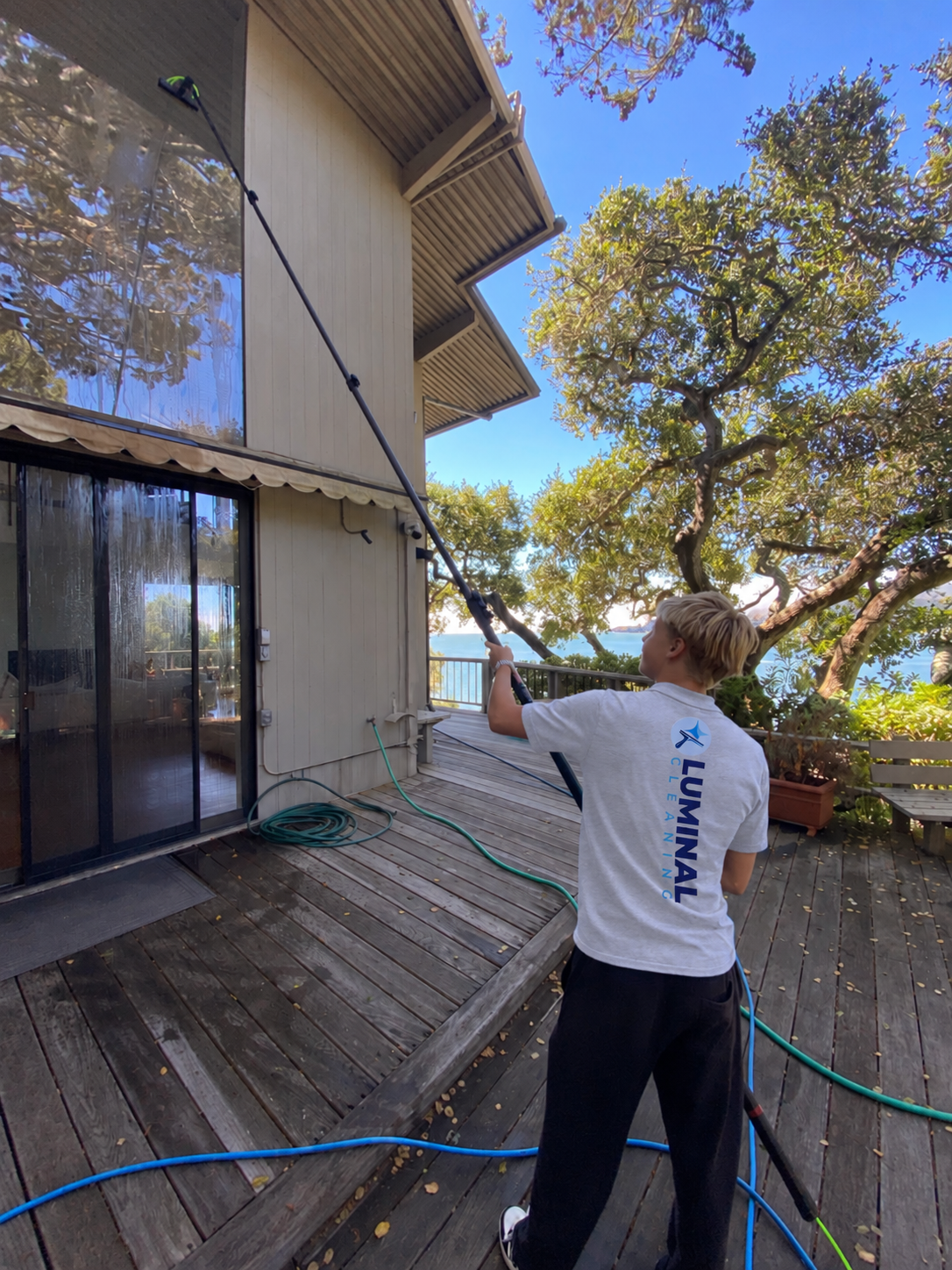 Luminal Cleaning technician using a long carbon water-fed pole to clean elevated exterior windows from the ground
